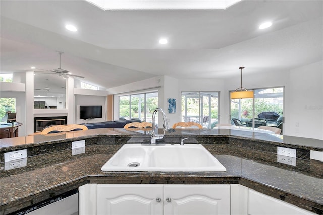 kitchen featuring open floor plan, dishwasher, vaulted ceiling, white cabinetry, and a sink