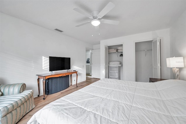 bedroom with a ceiling fan, visible vents, wood finished floors, and multiple closets