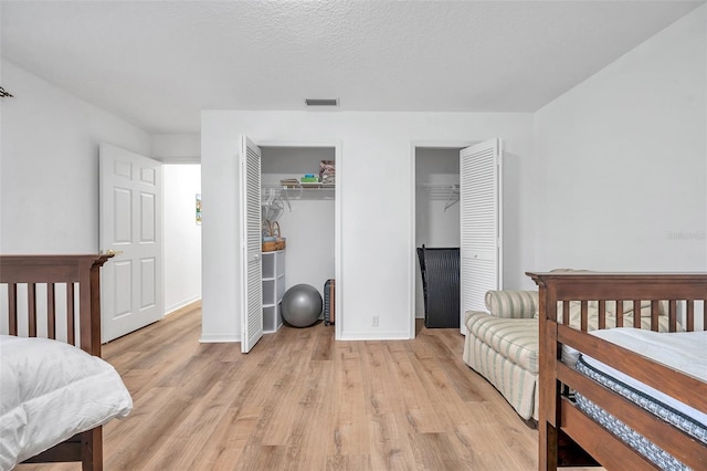 bedroom featuring visible vents, multiple closets, a textured ceiling, light wood-style floors, and baseboards