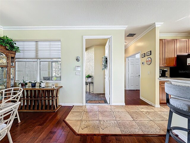 interior space with light wood finished floors, visible vents, a textured ceiling, and ornamental molding