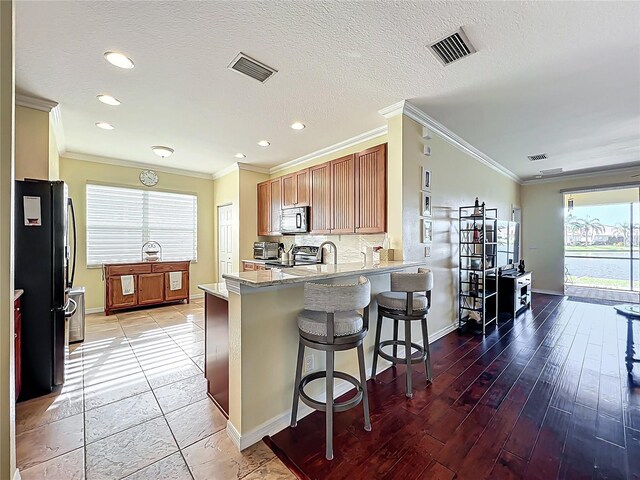 kitchen with stainless steel microwave, visible vents, a peninsula, freestanding refrigerator, and electric range