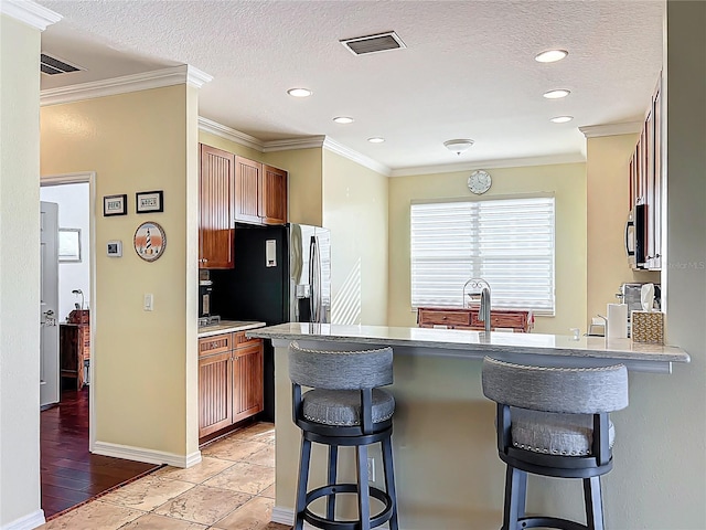 kitchen with a kitchen breakfast bar, black appliances, crown molding, and a textured ceiling