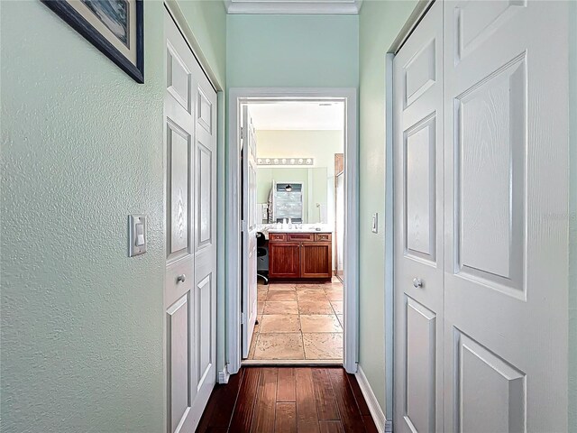 hallway with wood finished floors, a textured wall, and ornamental molding