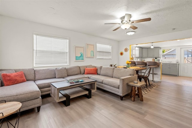 living room with a ceiling fan, a healthy amount of sunlight, light wood-style floors, and a textured ceiling