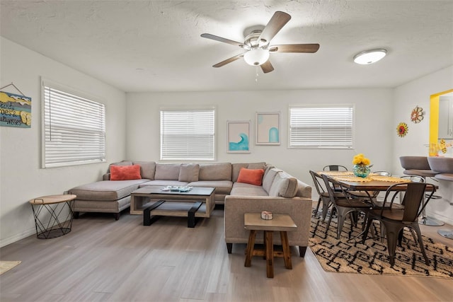 living area featuring light wood finished floors, a healthy amount of sunlight, a textured ceiling, and a ceiling fan