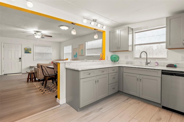 kitchen featuring a peninsula, a sink, gray cabinetry, light wood-style floors, and dishwasher