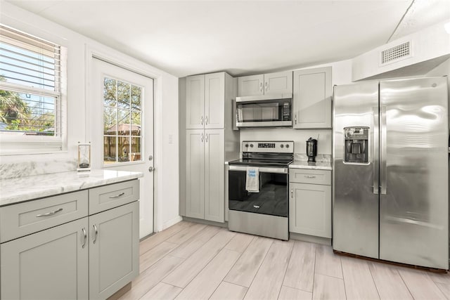 kitchen featuring wood finish floors, visible vents, gray cabinetry, light stone counters, and appliances with stainless steel finishes