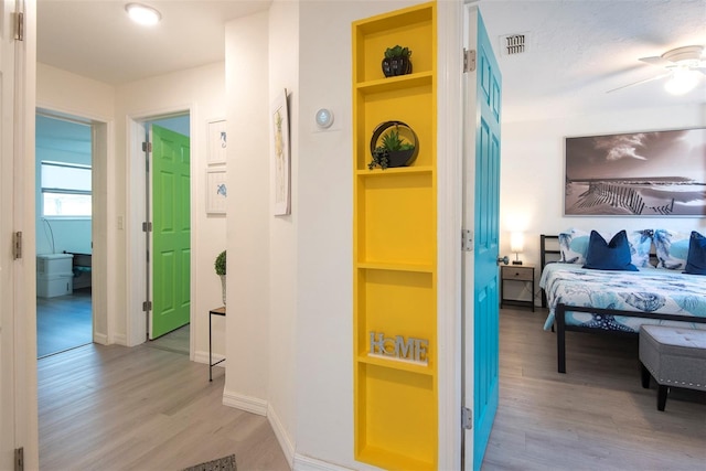 hall with light wood-type flooring, visible vents, baseboards, and built in features