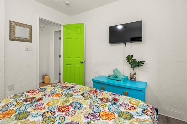 bedroom with wood finished floors, baseboards, and a textured wall