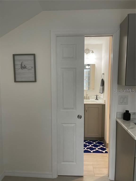 bathroom with baseboards, vanity, lofted ceiling, and wood finished floors