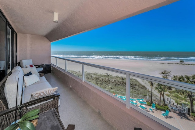 balcony with a water view, a sunroom, and a view of the beach