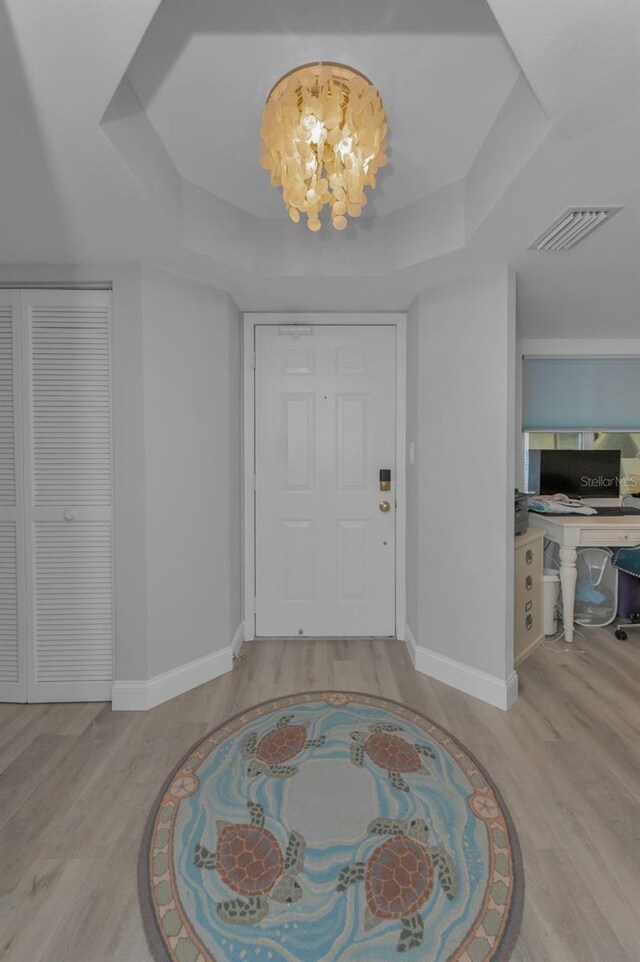 foyer entrance featuring a tray ceiling, a notable chandelier, visible vents, wood finished floors, and baseboards