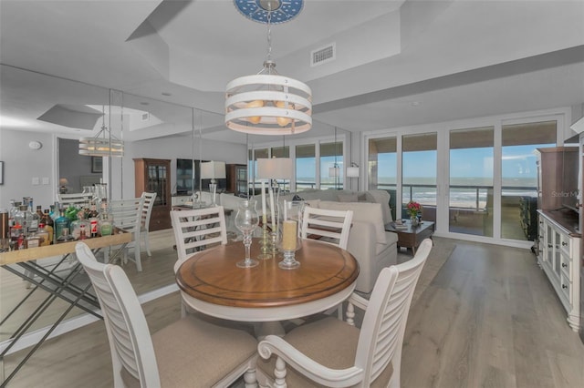 dining room featuring a tray ceiling, visible vents, a water view, and wood finished floors