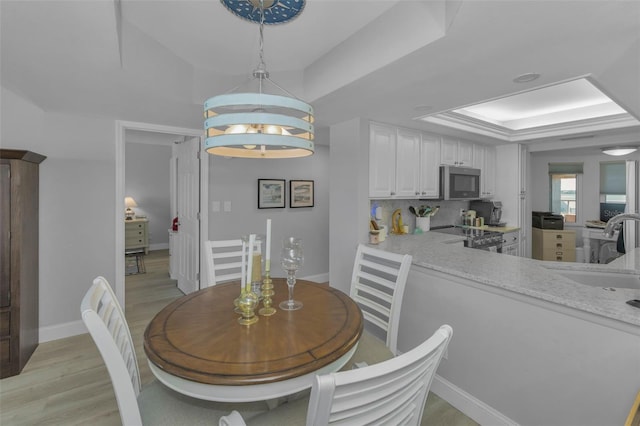 dining room featuring light wood-style flooring, baseboards, a raised ceiling, and a notable chandelier