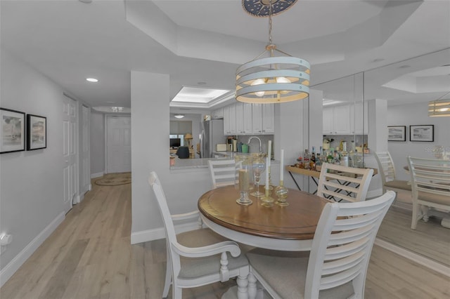 dining room featuring light wood finished floors, baseboards, a raised ceiling, and recessed lighting