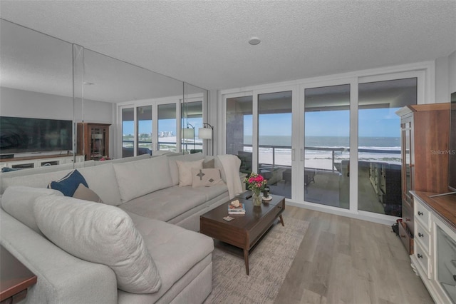 living room featuring expansive windows, light wood finished floors, a textured ceiling, and a water view