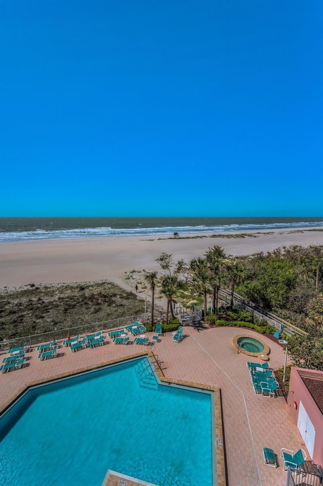 community pool featuring a patio, a water view, fence, a community hot tub, and a view of the beach