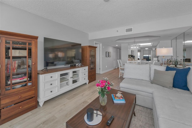 living room featuring visible vents, light wood-style floors, a textured ceiling, a chandelier, and baseboards