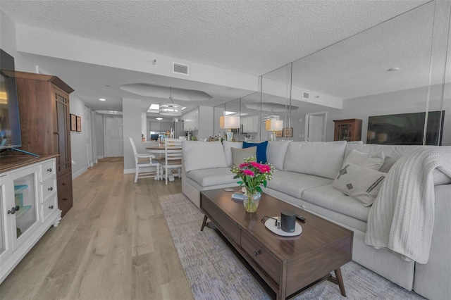 living area with a textured ceiling, a notable chandelier, visible vents, baseboards, and light wood-style floors