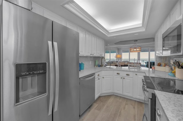 kitchen featuring white cabinets, a tray ceiling, stainless steel appliances, light wood-type flooring, and a sink