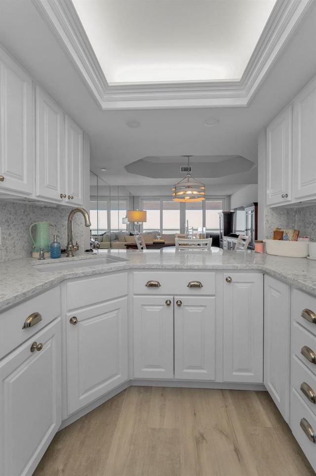 kitchen with a sink, white cabinetry, light wood-type flooring, decorative backsplash, and a raised ceiling