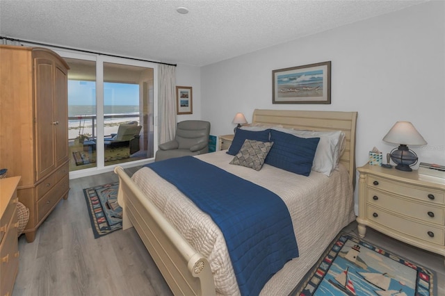 bedroom with a textured ceiling, a water view, wood finished floors, access to exterior, and floor to ceiling windows