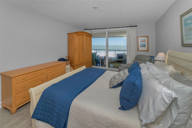 bedroom with light wood-type flooring, a water view, access to outside, and a textured ceiling