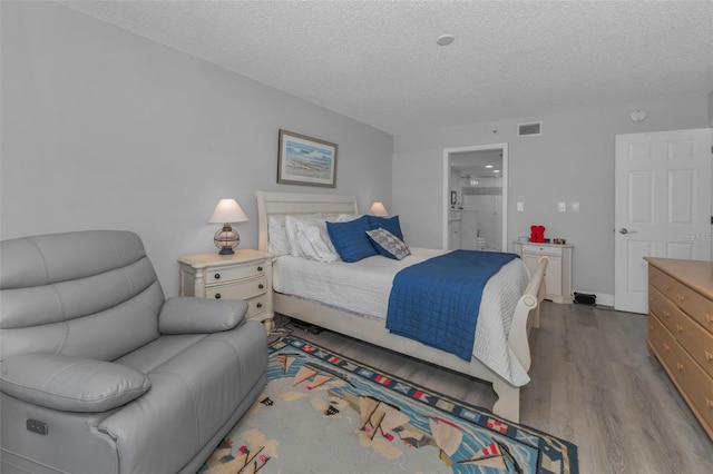 bedroom with a textured ceiling, visible vents, wood finished floors, and ensuite bathroom