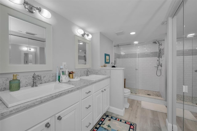 full bathroom with double vanity, a sink, a shower stall, and wood finished floors