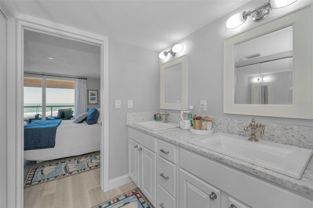 ensuite bathroom featuring connected bathroom, wood finished floors, a sink, and double vanity