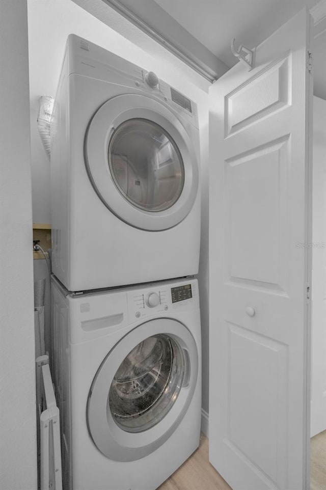 laundry room featuring laundry area, light wood-style flooring, and stacked washing maching and dryer