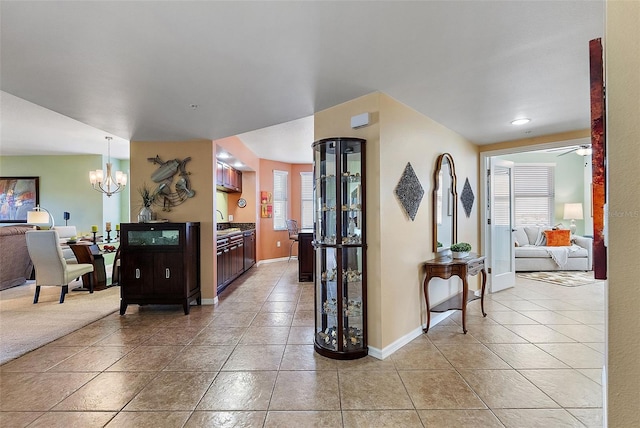 corridor with light tile patterned floors, a notable chandelier, baseboards, and a sink