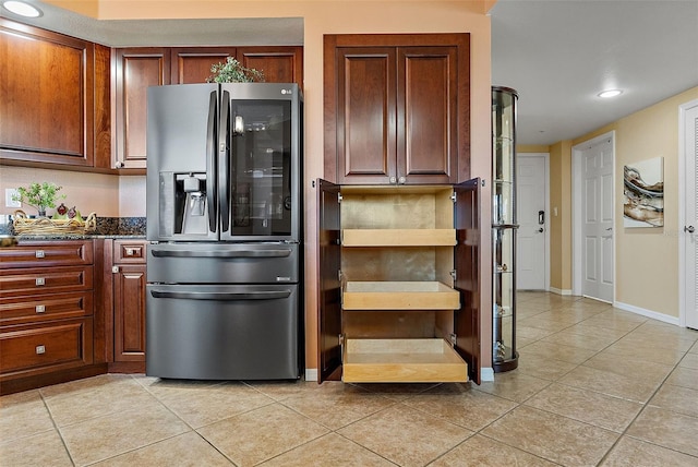 kitchen featuring light tile patterned floors, baseboards, stainless steel fridge, and dark stone countertops