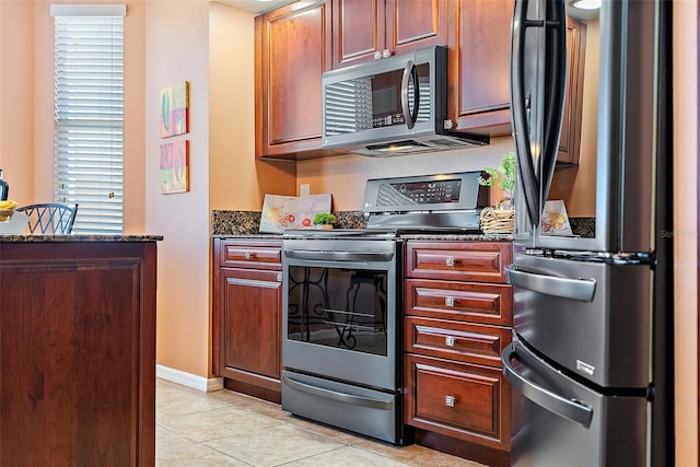 kitchen with dark stone counters, light tile patterned floors, and appliances with stainless steel finishes