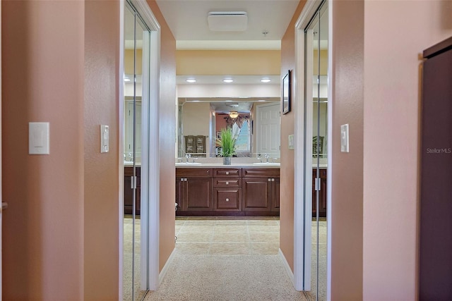 hall with a sink, baseboards, and light carpet