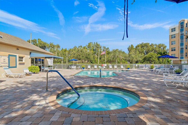 pool with a patio, a community hot tub, and fence