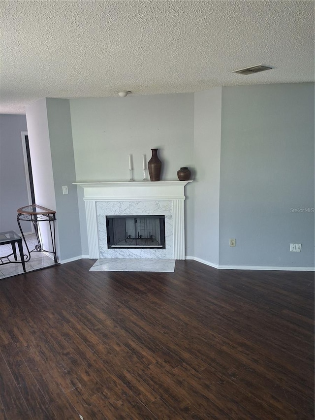 unfurnished living room featuring visible vents, a premium fireplace, a textured ceiling, wood finished floors, and baseboards