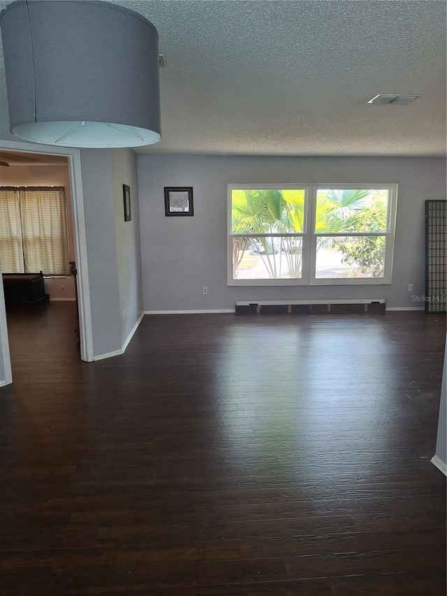 unfurnished room featuring baseboards, visible vents, dark wood finished floors, and a textured ceiling