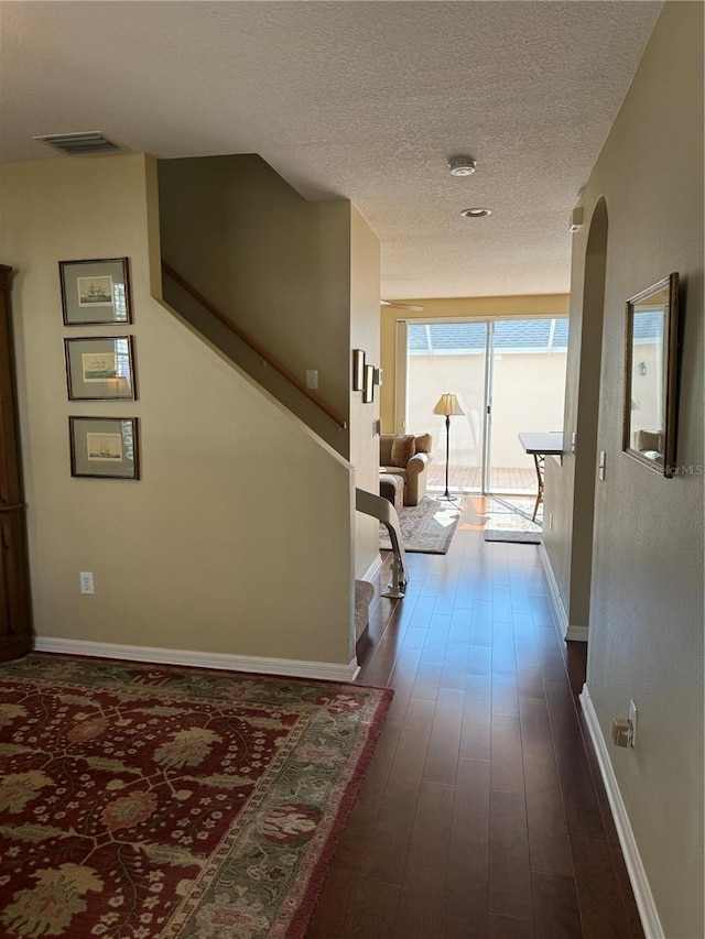 corridor featuring baseboards, a textured ceiling, visible vents, and dark wood-style flooring