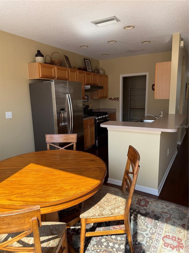 kitchen featuring black gas range, under cabinet range hood, a sink, visible vents, and stainless steel fridge with ice dispenser