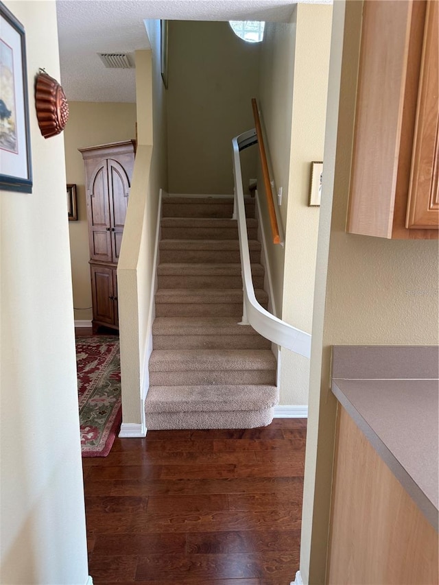 stairs featuring visible vents, a textured ceiling, baseboards, and wood finished floors