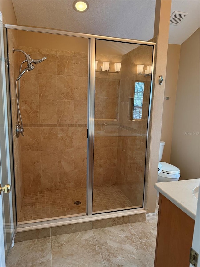 bathroom featuring a textured ceiling, toilet, visible vents, vanity, and a shower stall