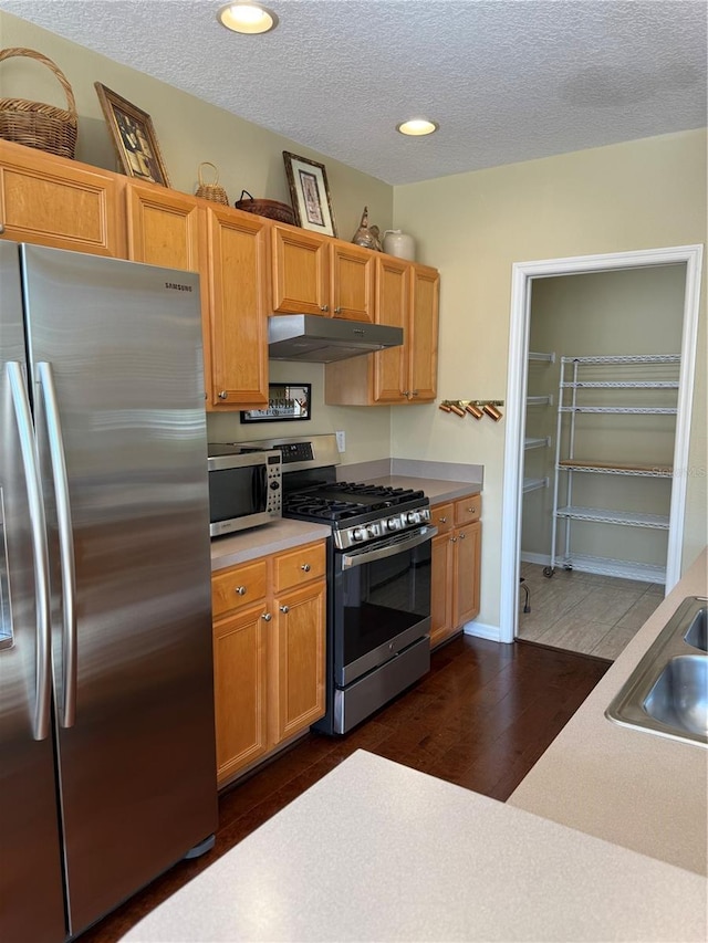 kitchen featuring dark wood-style flooring, stainless steel appliances, light countertops, under cabinet range hood, and a sink