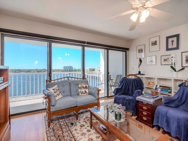 living area with a water view, wood finished floors, and a ceiling fan