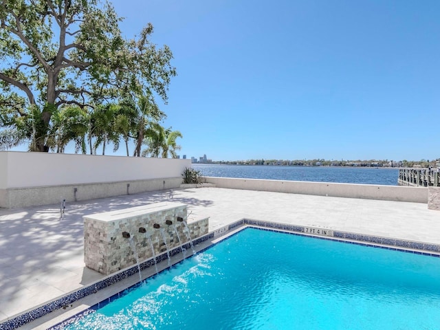 pool with a patio area, a water view, and fence