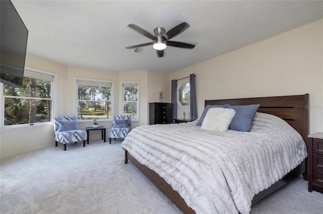 bedroom featuring visible vents, light colored carpet, a textured ceiling, and a ceiling fan