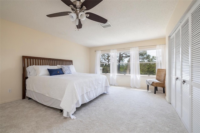 carpeted bedroom with visible vents, a textured ceiling, and a ceiling fan