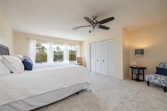 carpeted bedroom with ceiling fan, visible vents, a closet, and a textured ceiling