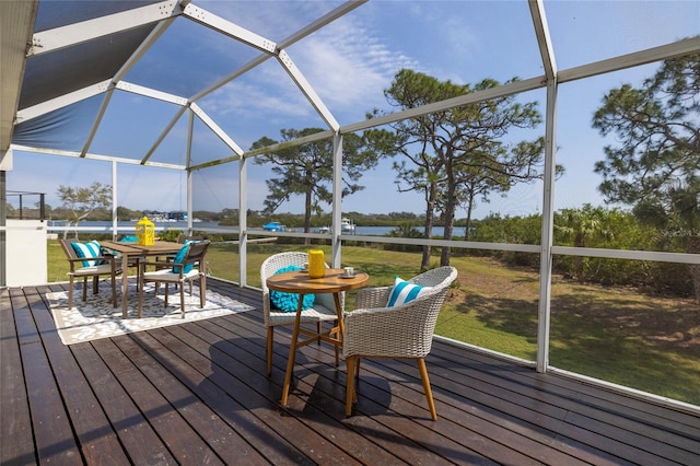 exterior space featuring glass enclosure, a lawn, outdoor dining area, and a water view