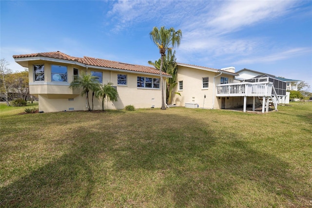 back of property featuring stucco siding, a lawn, a deck, and a tile roof